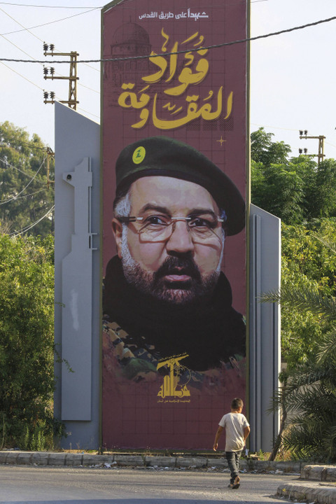 Seorang anak laki-laki berjalan melewati poster yang menggambarkan komandan Hizbullah yang terbunuh, Fuad Shukr, di kota selatan Lebanon, Sidon (25/8/2024). Foto: Anwar Amro/AFP
