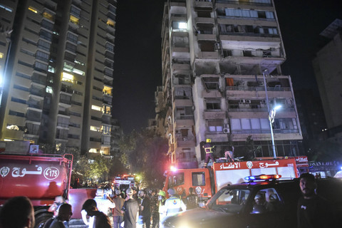 Petugas pemadam kebakaran berkumpul di lokasi gedung apartemen yang terkena serangan udara Israel di distrik Cola, Beirut, Minggu (30/9/2024). Foto: FADEL ITANI/AFP