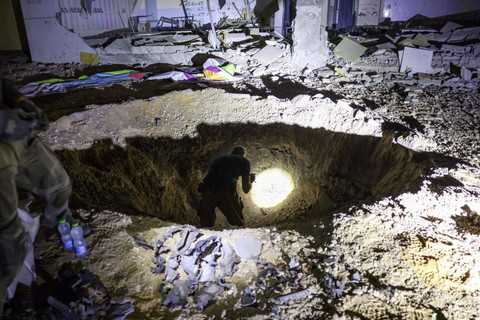 Anggota Komando Front Dalam Negeri Israel dan pasukan polisi memeriksa kawah setelah serangan rudal Iran ke wilayah Israel di kota Gedera, Israel, Rabu (2/10/2024). Foto: MENAHEM KAHANA / AFP