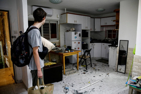 Warga berdiri di dekat rumah yang terkena dampak jatuhnya proyektil di Haifa, Israel utara, Senin (7/10/2024). Foto: Shir Torem/REUTERS