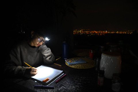 Seorang siswa menggunakan lampu kepala belajar saat terjadi pemadaman listrik di Quito, Ekuador. Foto: RODRIGO BUENDIA / AFP
