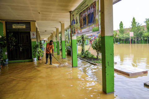 Penjaga sekolah berusaha membuang air yang menggenangi lorong sekolah karena terdampak banjir di SMPN 1 Bojongsoang, Kabupaten Bandung, Jawa Barat, Minggu (24/11/2024). Foto: Raisan Al Farisi/ANTARA FOTO