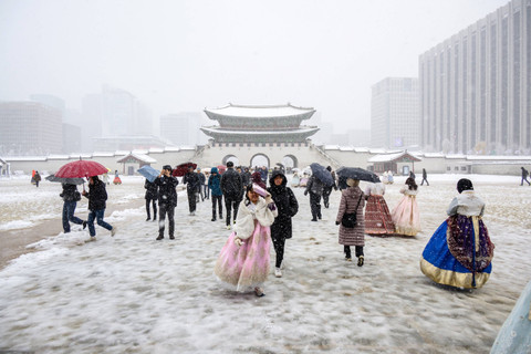 Pengunjung yang mengenakan pakaian tradisional hanbok terlihat di halaman Istana Gyeongbokgung di tengah hujan salju lebat di pusat kota Seoul, Korea Selatan, Rabu (27/11/2024). Foto: ANTHONY WALLACE / AFP