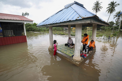 Sebuah keluarga duduk di pergola yang dikelilingi oleh air banjir di Pasir Mas di negara bagian Kelantan, Malaysia utara pada tanggal 21 Desember 2022. Foto: STR/AFP