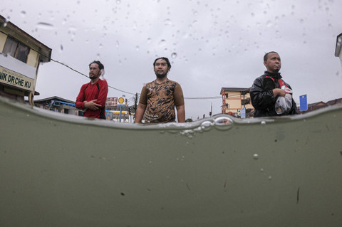 Tiga warga melintasi banjir di Negara Bagian Kelantan, Malaysia, Sabtu (30/11/2024). Foto: Mohd RASFAN/AFP