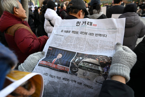 Seorang pria membaca koran edisi tambahan yang dipajang di gerbang kereta bawah tanah di pusat kota Seoul, Korea Selatan, Rabu (4/12/2024). Foto: Jung Yeon-je / AFP