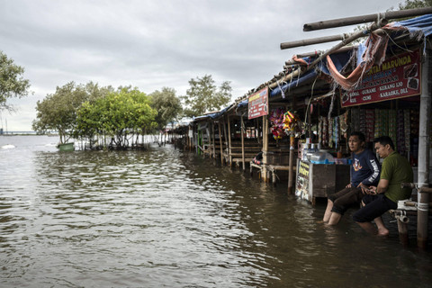 Dua pengunjung duduk di warung saat banjir rob di kawasan Pantai Marunda, Jakarta, Rabu (4/12/2024). Foto: Aprillio Akbar/ANTARA FOTO