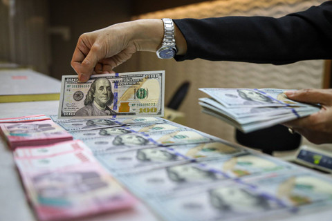 Seorang petugas menunjukan pecahan Dolar AS dan Rupiah di salah satu tempat penukaran mata uang asing di Kwitang, Jakarta, Senin (9/12/2024). Foto: Iqbal Firdaus/kumparan