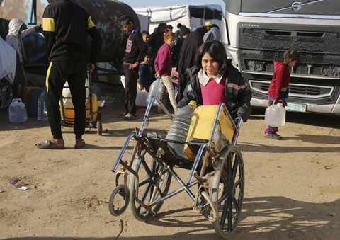 Seorang anak Palestina membawa galon berisi air bersih menggunakan kursi roda di Khan Younis, Gaza, Kamis (19/12/2024). Foto: Hatem Khaled/REUTERS