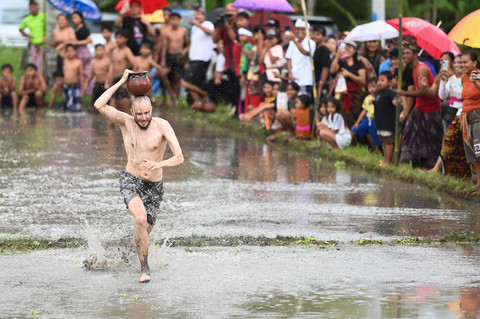 Wisatawan mancanegara berlari sambil menjunjung tembikar saat mengikuti lomba permainan tradisional di area persawahan Desa Suwat, Gianyar, Bali, Senin (30/12/2024). Foto: ANTARA FOTO/Fikri Yusuf