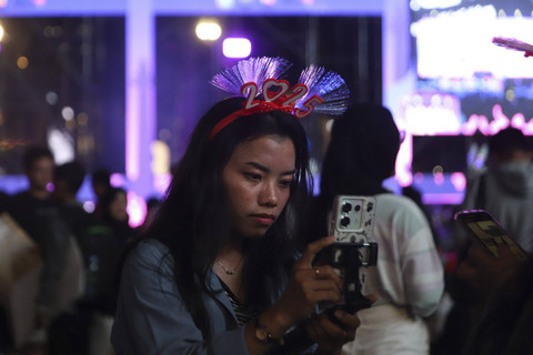 Seorang warga menggunakan ponsel pintarnya saat menyaksikan malam pergantian tahun baru 2025 di kawasan Bundaran HI, Jakarta, Selasa (31/12/2024). Foto: Iqbal Firdaus/kumparan