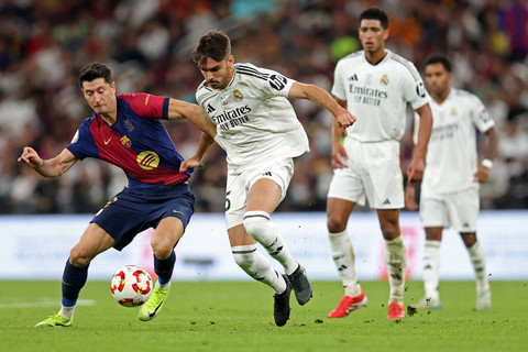 Pemain FC Barcelona Robert Lewandowski berebut bola dengan pemain Real Madrid Raul Asencio pada pertandingan final Piala Super Spanyol di King Abdullah Sport City, Jeddah, Arab Saudi, Minggu (12/1/2025). Foto: Haitham AL-SHUKAIRI / AFP