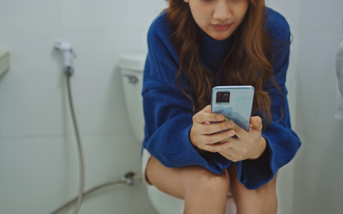 Ilustrasi perempuan bermain hp terlalu lama di toilet. Foto: Shutterstock