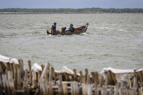 Seorang nelayan mengendarai perahu di antara pagar laut. Foto: Iqbal Firdaus/kumparan