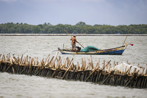 Seorang nelayan mengendarai perahu diantara pagar laut. Foto: Iqbal Firdaus/kumparan