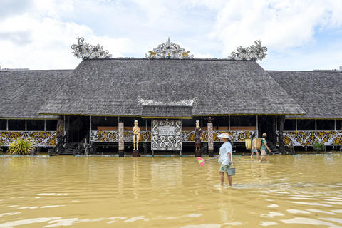 Warga berjalan melintasi banjir di halaman Lamin Adat Pemung Tawai, Desa Budaya Adat Pampang, Samarinda, Kalimantan Timur, Senin (27/1/2025). Foto: M Risyal Hidayat/ANTARA FOTO