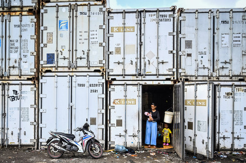Pengungsi menggendong anaknya di dalam kontainer kosong di Rorotan, Jakarta, Jumat (31/1/2025).  Foto: ANTARA FOTO/Rivan Awal Lingga