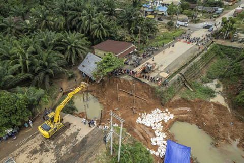 Foto udara warga menyaksikan pekerja memasang tiang penyangga jembatan darurat menggunakan alat berat di Jalan Lintas Sumatera yang amblas, Desa Sirih Sekapur, Bungo, Jambi, Kamis (6/3/2025). Foto: Wahdi Septiawan/ANTARA FOTO