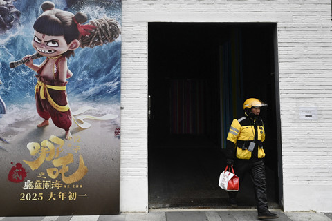 Seorang pengantar makanan berjalan di samping promosi film animasi Tiongkok Ne Zha 2, yang diproduksi oleh Enlight Media, di luar kantor pusat perusahaan produksi tersebut di Beijing, Cihna (11/2/2025). Foto: Pedro Pardo/AFP