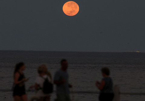 Bulan purnama terbenam selama gerhana bulan total, saat orang-orang berjalan di kawasan pejalan kaki Sea Point, di Cape Town, Afrika Selatan, 14 Maret 2025. Foto: REUTERS/Esa Alexander