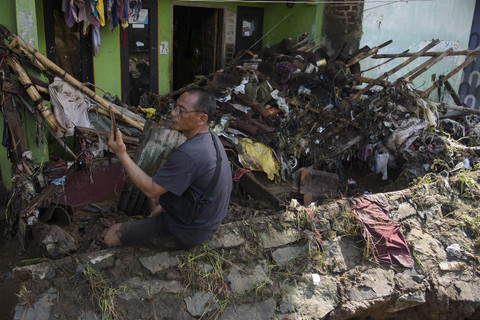 Warga menggunakan gawai di depan rumah yang rusak terdampak banjir akibat tanggul Sungai Cigede jebol di Desa Citeureup, Kabupaten Bandung, Jawa Barat, Minggu (16/3/2025). Foto: Novrian Arbi/ANTARA FOTO