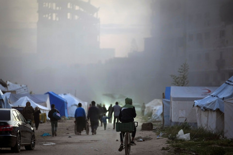 Warga melewati asap mengepul dari sebuah gedung setelah menjadi sasaran serangan tentara Israel di Kota Gaza, Sabtu (22/3/2025). Foto: Jehad Alshrafi/AP Photo