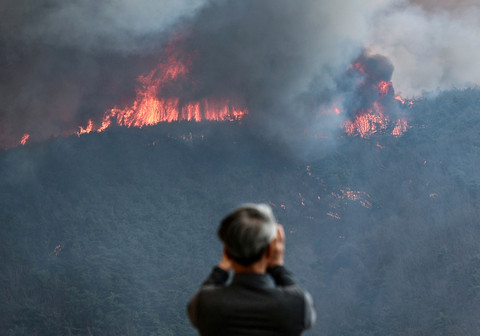 Seorang warga merekam kebakaran hutan yang menghancurkan sebuah gunung di Uiseong, Korea Selatan, 24 Maret 2025. Foto: Yonhap via REUTERS