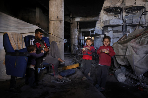 Warga Palestina duduk bersama anak-anaknya di dalam auditorium kampus Universitas Islam yang rusak di Kota Gaza, Rabu (16/4/2025). Foto: Bashar Taleb/AFP