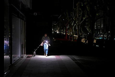 Seorang wanita menggunakan senter ponselnya saat mengajak anjingnya jalan-jalan saat jalanan gelap selama pemadaman listrik besar-besaran di Vigo, Spanyol, Senin (28/4/2025). Foto: Miguel Riopa/AFP