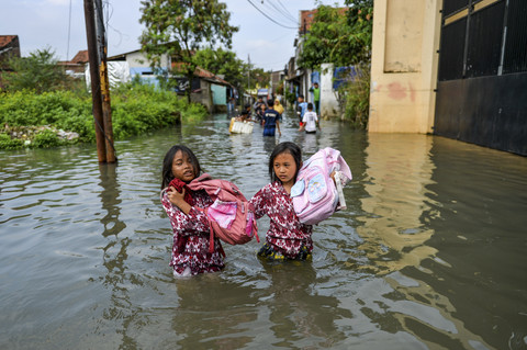Dua siswi sekolah dasar melintasi banjir yang menggenangi permukiman di Kampung Bojongasih, Dayeuhkolot, Kabupaten Bandung, Jawa Barat, Jumat (16/5/2025). Foto: Raisan Al Farisi/ANTARA FOTO