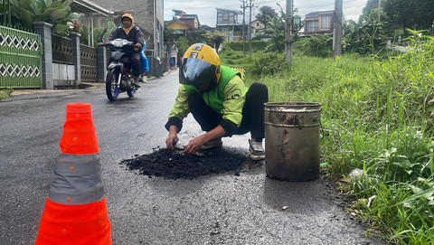 Pengemudi ojek online, Hasan Fiidel, menambal jalan rusak di Kabupaten Bandung. Foto: kumparan