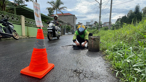 Pengemudi ojek online, Hasan Fiidel, menambal jalan rusak di Kabupaten Bandung. Foto: kumparan
