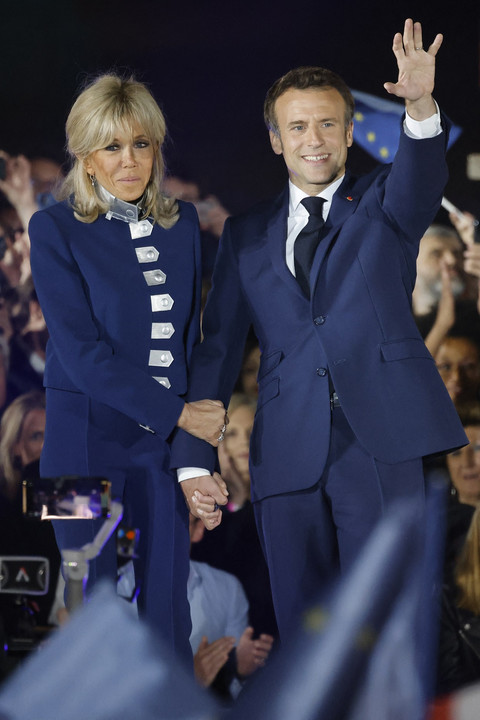 Presiden Prancis sekaligus kandidat petahana dari partai La République en Marche (LREM), Emmanuel Macron (kanan), melambaikan tangan sambil menggenggam tangan Brigitte Macron saat merayakan kemenangannya dalam putaran kedua pemilihan presiden Prancis di Champ de Mars, Paris, pada 24 April 2022. Foto: AFP