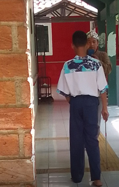 Siswa tunametra SLB Negeri Semarang meraba-raba blok pemandu dengan ujung tongkatnya. Seorang guru (mengenakan blangkon) berada di deoannga, memandu dengan instruksi verbal berseling bunyi kelintingan di salah satu sudut sekolah, baru-baru inj. (Foto: Mohamad Jokomono)