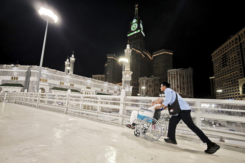 Petugas layanan lansia PPIH Arab Saudi Abdurrahman mendorong kursi roda yang dinaiki calon haji lansia Soemarno di Masjidil Haram untuk menunaikan umrah wajib. Foto: Andika Wahyu/ANTARA FOTO