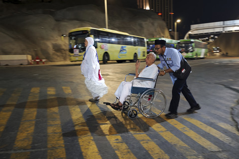 Petugas layanan lansia PPIH Arab Saudi Abdurrahman (kanan) membisikkan kalimat talbiyah sambil mendorong kursi roda yang dinaiki calon haji lansia Soemarno menuju Masjidil Haram untuk menunaikan umrah wajib. Foto: Andika Wahyu/ANTARA FOTO