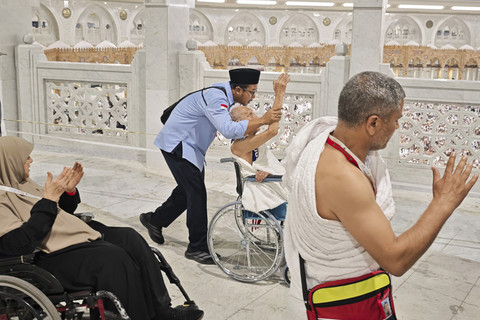 Petugas layanan lansia PPIH Arab Saudi Abdurrahman membisikkan doa dan mengangkat tangan calon haji lansia Soemarno saat tawaf melewati rukun Hajar Aswad dalam rangkaian umrah wajib di Masjidil Haram. Foto: Andika Wahyu/ANTARA FOTO