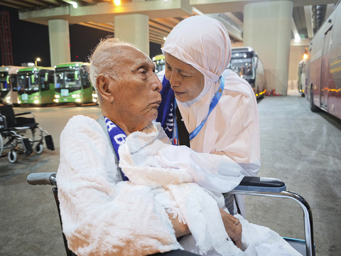 Petugas layanan lansia PPIH Arab Saudi Abdurrahman mendorong kursi roda yang dinaiki calon haji lansia Soemarno di Masjidil Haram untuk menunaikan umrah wajib. Foto: Andika Wahyu/ANTARA FOTO