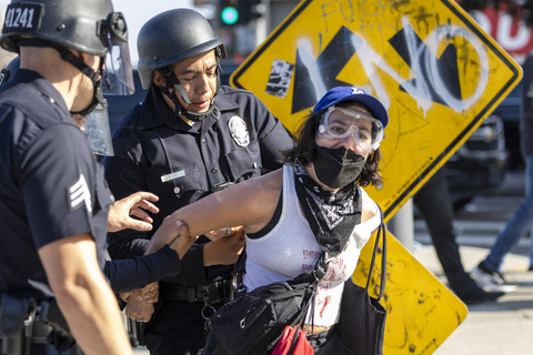 Seorang wanita ditangkap, ketika para pengunjuk rasa bentrok dengan aparat keamanan saat melakukan aksi protes menentang razia imigrasi federal di pusat kota Los Angeles, California, Minggu (8/6/2025). Foto: Ringo Chiu/AFP