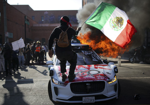 Seorang demonstran melambaikan bendera Meksiko sambil berdiri di atas mobil dalam aksi protes menentang razia imigrasi federal di pusat kota Los Angeles, California, AS, Minggu (8/6/2025). Foto: Daniel Cole/REUTERS