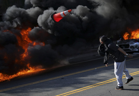 Seorang demonstran melempar kerucut lalu lintas saat api menyala selama protes terhadap razia imigrasi federal di pusat kota Los Angeles, California, AS, Minggu (8/6/2025). Foto: Daniel Cole/REUTERS