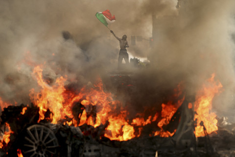 Seorang pria melambaikan bendera Meksiko saat asap dan api membumbung dari sebuah kendaraan yang terbakar dalam sebuah protes menentang razia imigrasi federal, di dekat Balai Kota Los Angeles di pusat kota Los Angeles, California, Minggu (8/6/2025). Foto: David Swanson/REUTERS