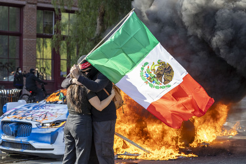 Sepasang suami istri berpelukan saat sebuah kendaraan Waymo terbakar, ketika para demonstran bentrok dengan penegak hukum di jalan di sekitar gedung federal di Los Angeles, California, AS, Minggu (8/6/2025). Foto: Ringo Chiu/AFP