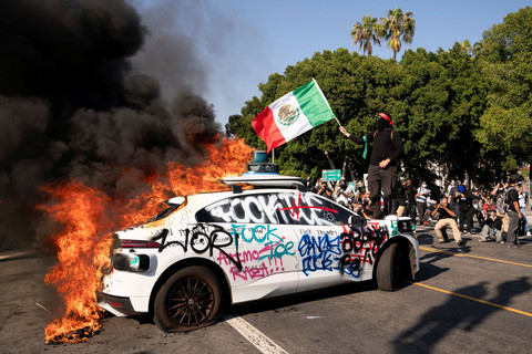 Vandalisme di kendaraan yang terbakar selama protes terhadap razia imigrasi federal di pusat kota Los Angeles, California, AS, Minggu (8/6/2025). Foto: David Ryder/REUTERS