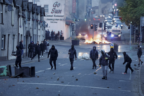 Orang-orang berjalan saat api membumbung tinggi saat kerusuhan malam kedua, di Ballymena, Irlandia Utara, Selasa (10/6/2025). Foto: Clodagh Kilcoyne/REUTERS