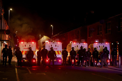 Petugas polisi berbaris di depan kendaraan yang terbakar saat kerusuhan malam kedua, di Ballymena, Irlandia Utara, Selasa (10/6/2025). Foto: Clodagh Kilcoyne/REUTERS