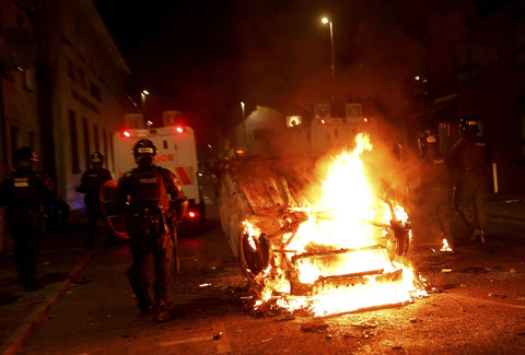 Petugas polisi beroperasi di dekat kendaraan yang terbakar saat kerusuhan malam kedua, di Ballymena, Irlandia Utara, Selasa (10/6/2025). Foto: Clodagh Kilcoyne/REUTERS