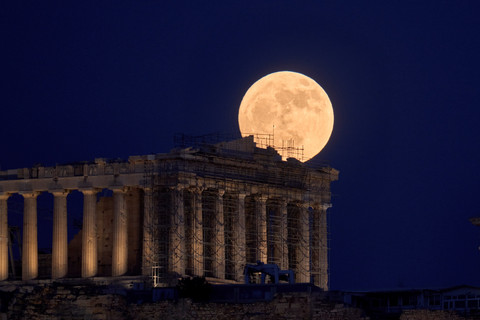 Bulan purnama yang dikenal sebagai 'Strawberry Moon' muncul di balik kuil Parthenon abad ke-5 SM di bukit Acropolis kuno, Athena, Selasa (10/6/2025). Foto: Petros Giannakouris/AP Photo