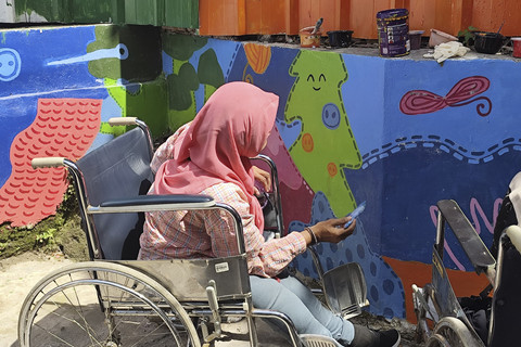 Linda (63), penyandang disabilitas daksa, saat melukis mural di Kampung Binong, Bandung, Jawa Barat, Sabtu (14/6/2025).  Foto: Alya Zahra/kumparan 