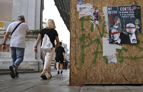 Sejumlah warga berjalan melewati sebuah poster yang menyerukan protes terhadap perang dan pernikahan pendiri Amazon, Jeff Bezos, di Venesia, Rabu (25/6/2025). Foto: Stefano Rellandini/AFP